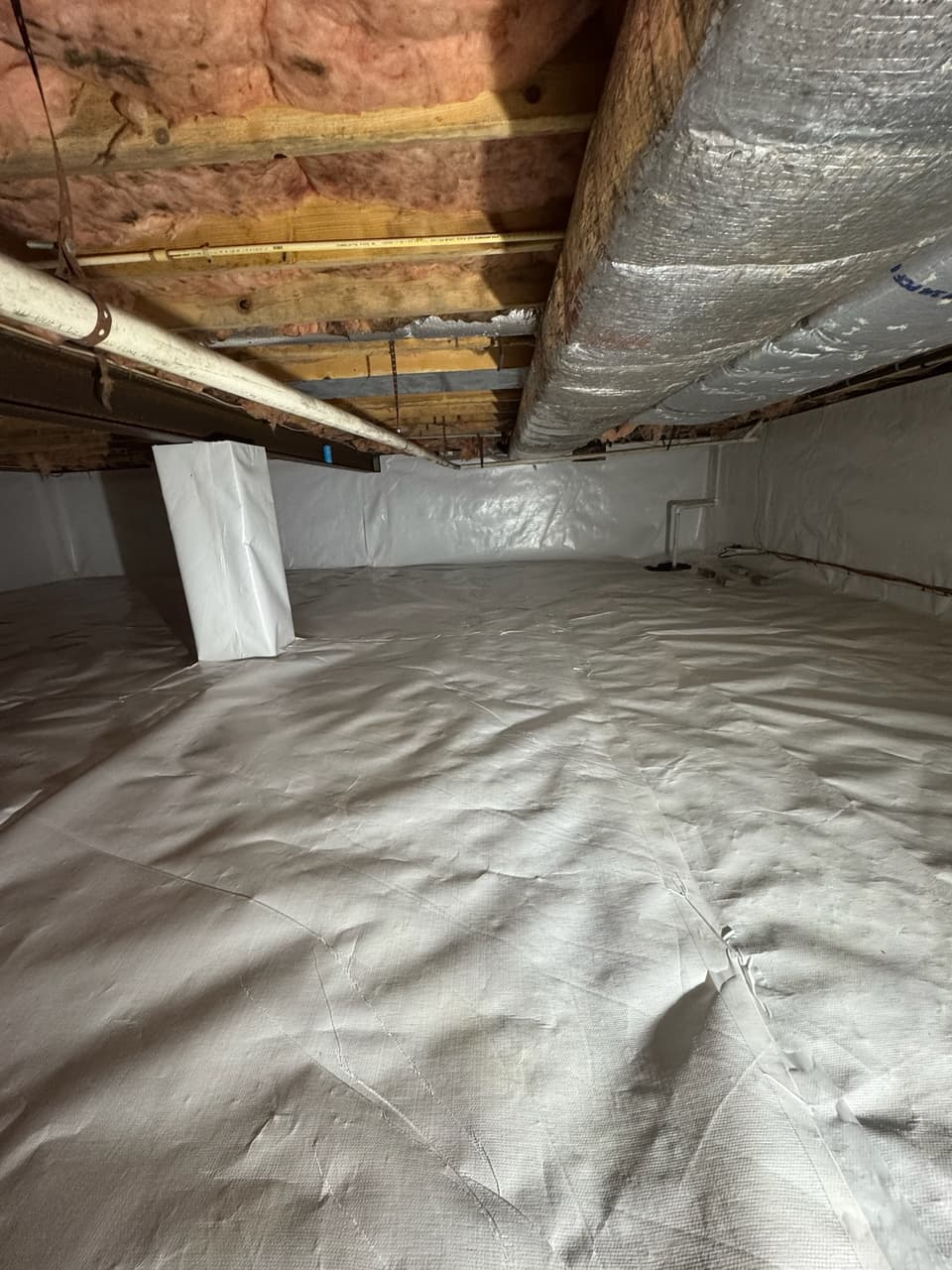Vapor barrier run up a crawl space wall beneath fiberglass insulated joists