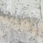 Weathered wall with chipped, peeling paint in beige, gray, and white tones revealing multiple layers and textures.